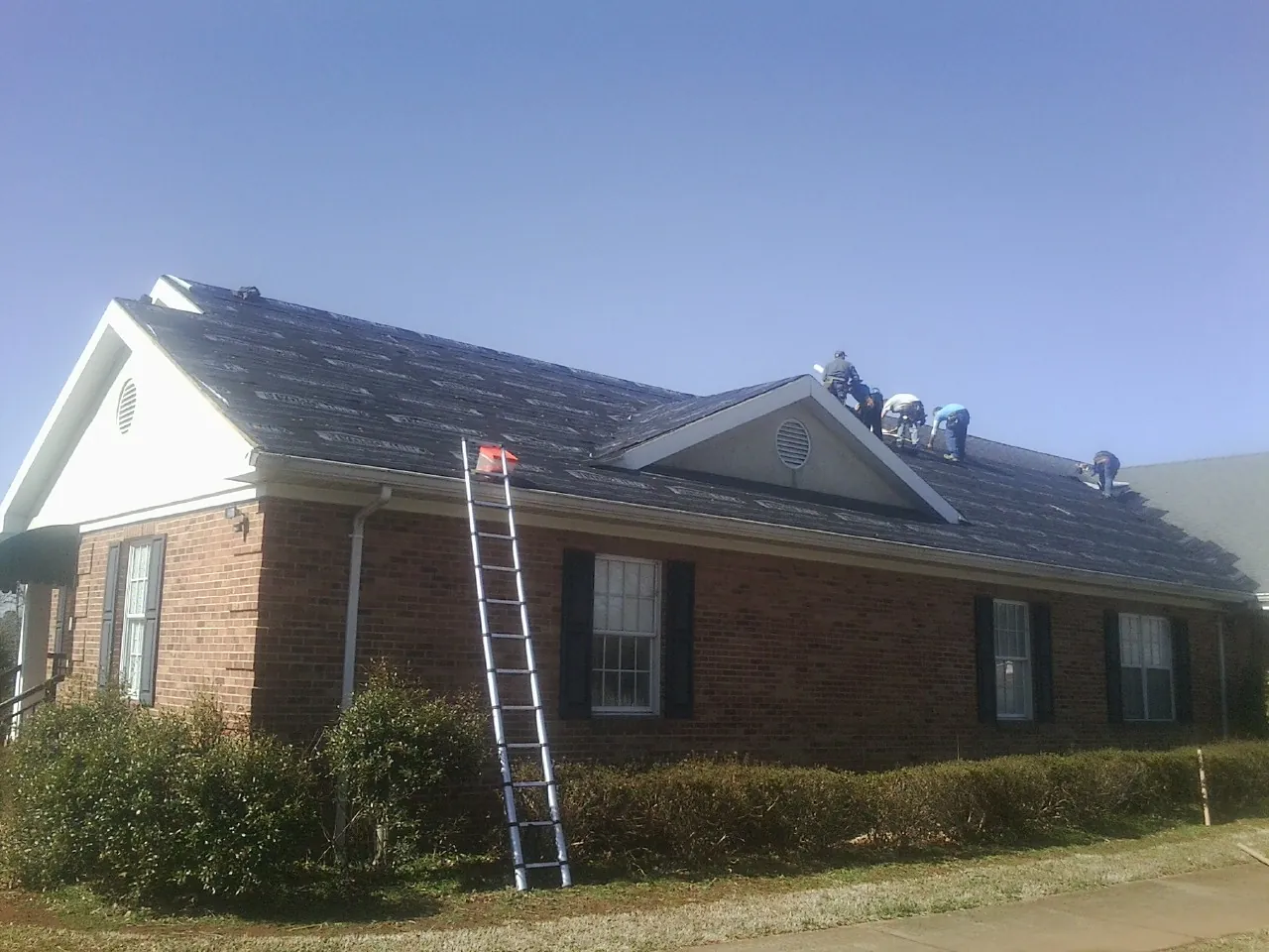 Crew tearing shingles off a brick ranch roof with a ladder set — Metal Roof Repair work by our crew in Valatie