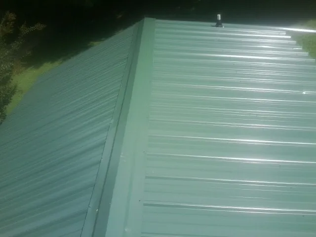 New green metal panels meeting at the ridge of a roof — Flat Roof Repair work by our crew in Valatie