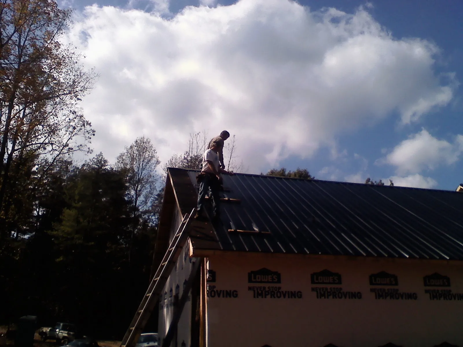 Roofer fastening dark metal panels high against a cloudy sky, from a Roof Inspection job in Valatie