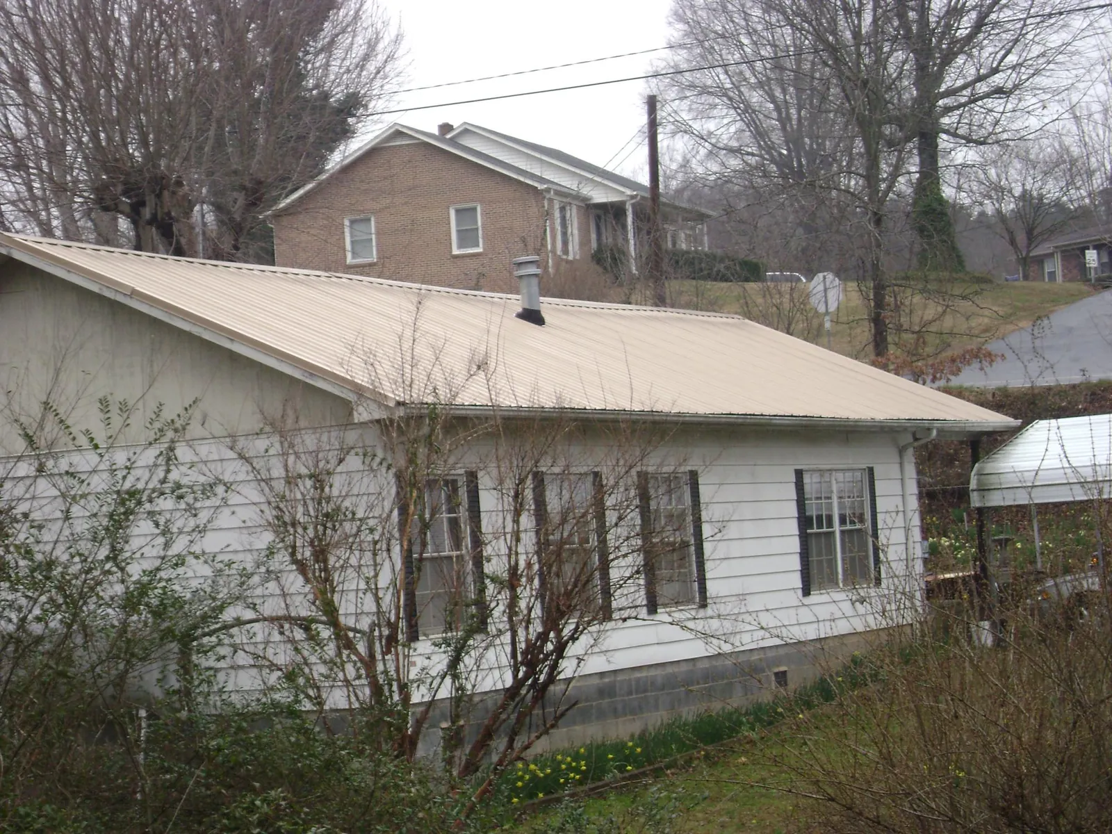 Tan metal roof on a white sided house set into a hillside — Commercial Roofing by Roofing Brothers in Valatie